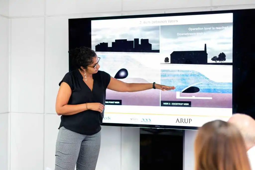 A woman pointing at the screen while giving a presentation.